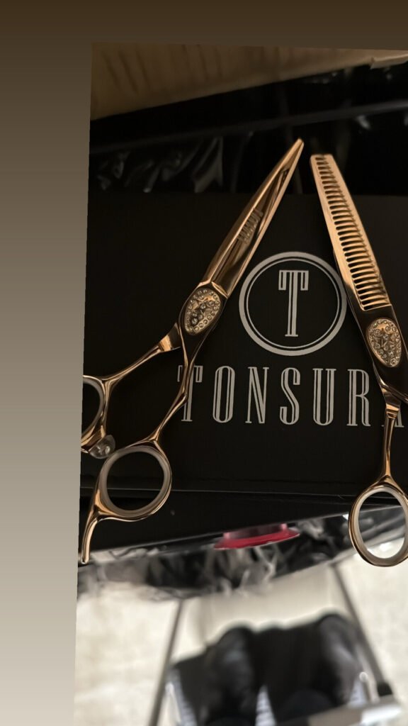Tijeras de barbero doradas y un peine sobre una caja negra con el logotipo TONSURA