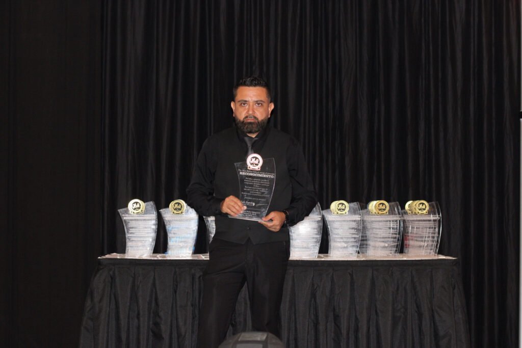 Luis Zepeda detrás de una mesa con trofeos y premios ante una cortina negra
