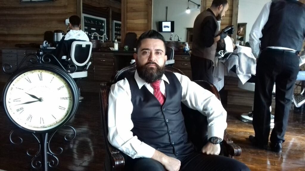 Interior de una barbería con un reloj de pared grande y un hombre sentado en el sillón