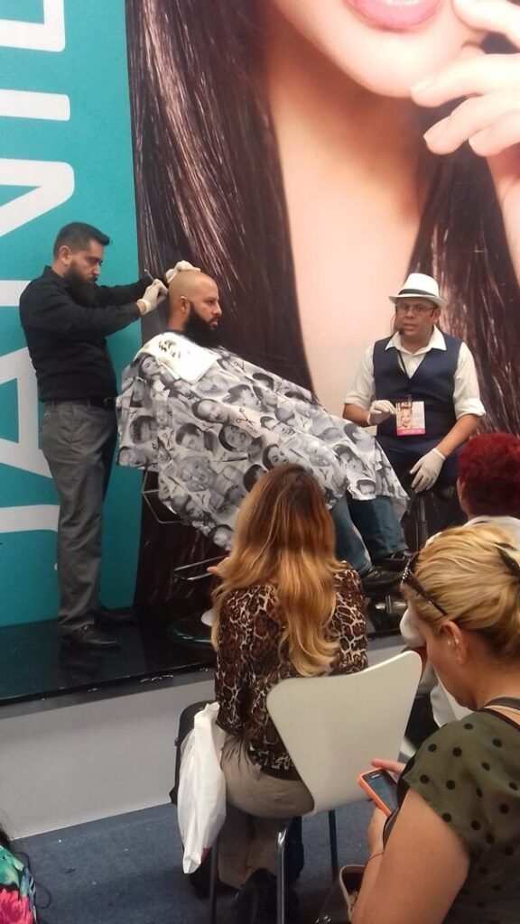 Barbero atendiendo a un cliente con capa durante una demostración ante el público