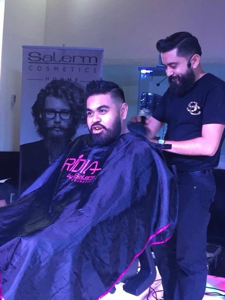 Barbero con máquina recortando el pelo a un cliente con capa Salerm